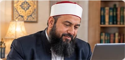 Qari Abdul Rahman, teaching at a laptop, a bookcase behind him